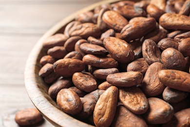 Bowl with cocoa beans on wooden table, closeup