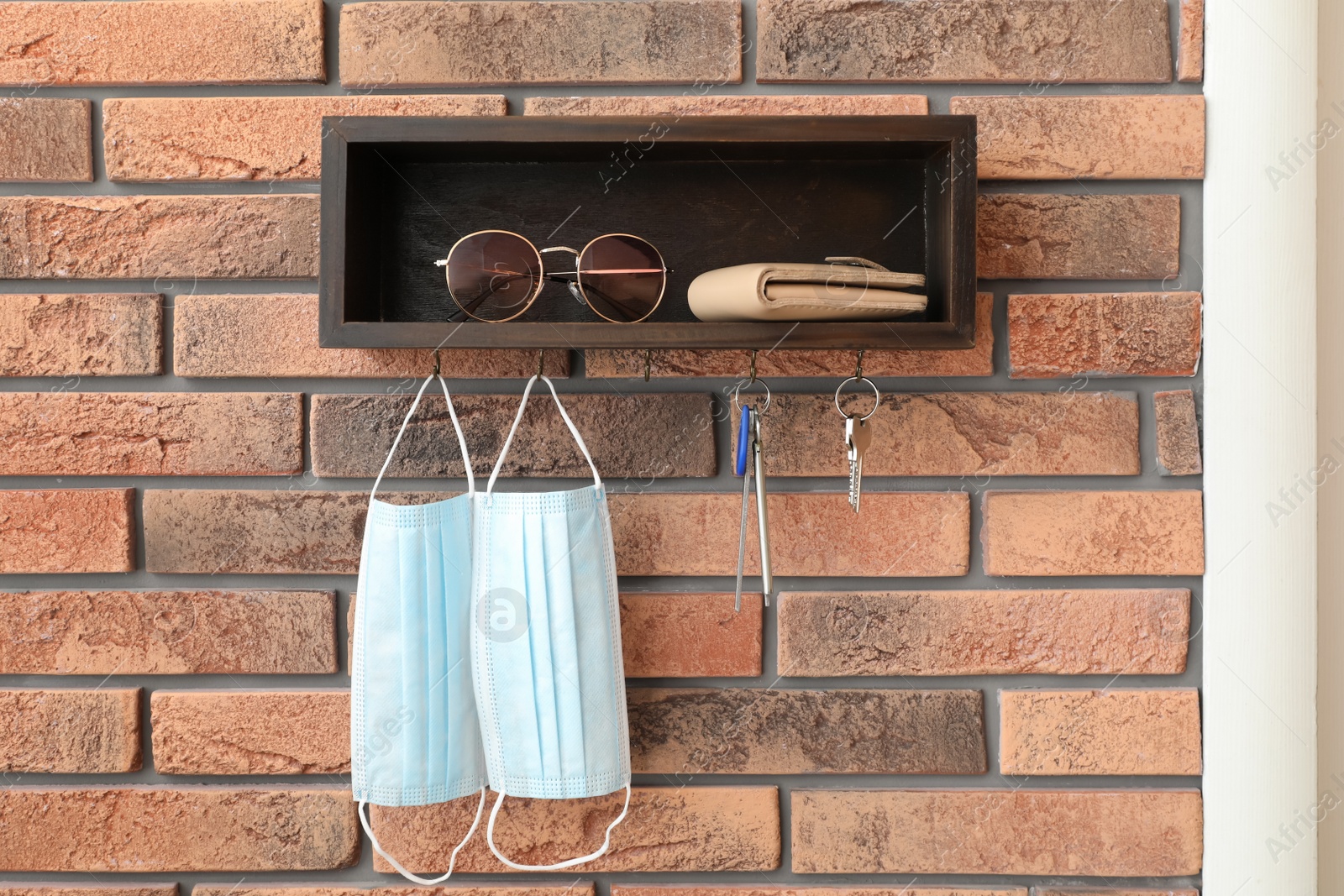 Photo of Hanger for keys with protective masks and accessories on brick wall