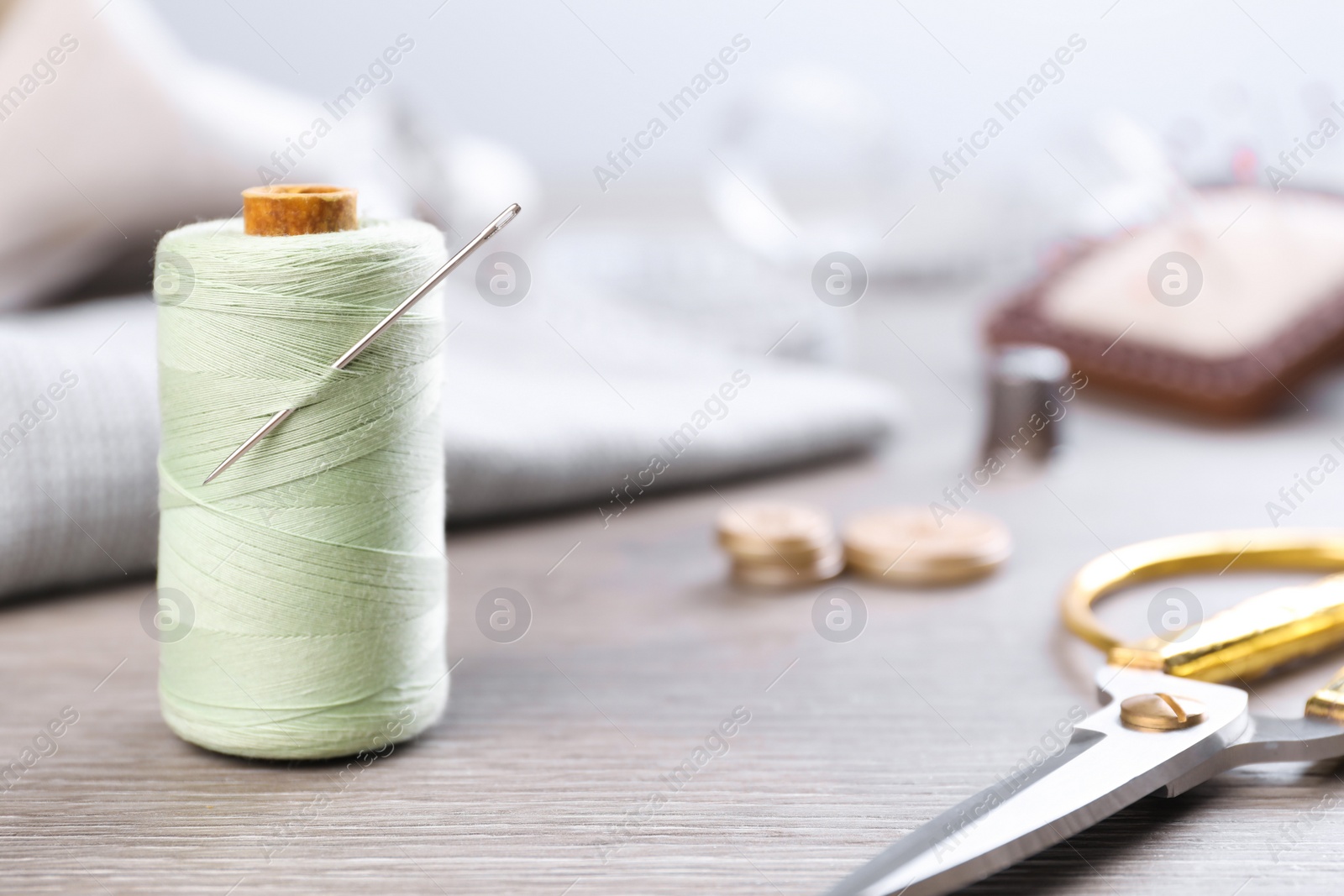 Photo of Spool of light green sewing thread with needle and scissors on wooden table, space for text