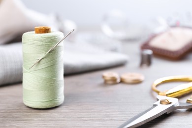 Photo of Spool of light green sewing thread with needle and scissors on wooden table, space for text