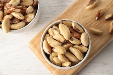 Photo of Bowls with tasty Brazil nuts on white wooden table, top view