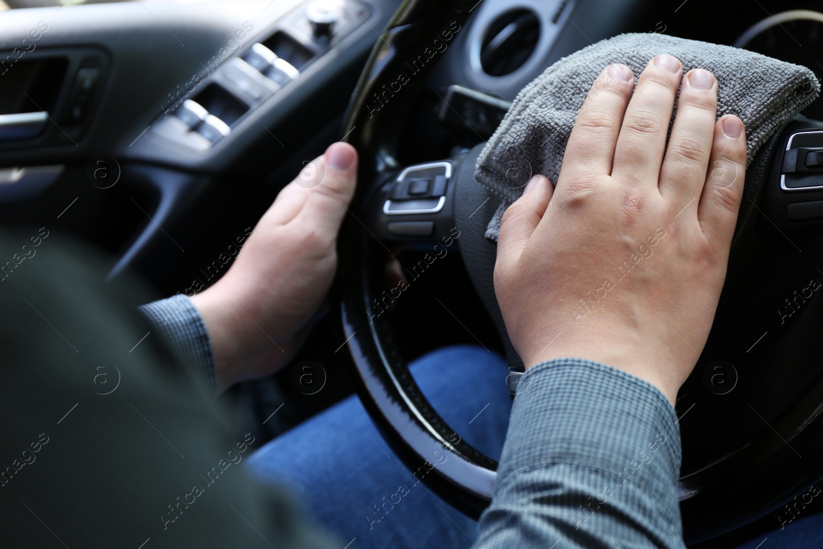 Photo of Man cleaning steering wheel with rag in car, closeup