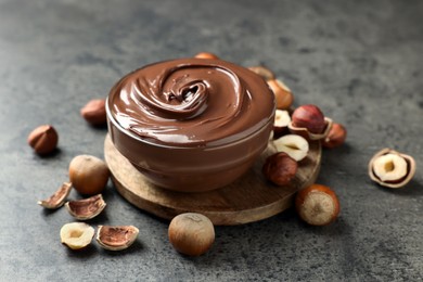 Glass bowl with tasty chocolate hazelnut spread and nuts on grey table