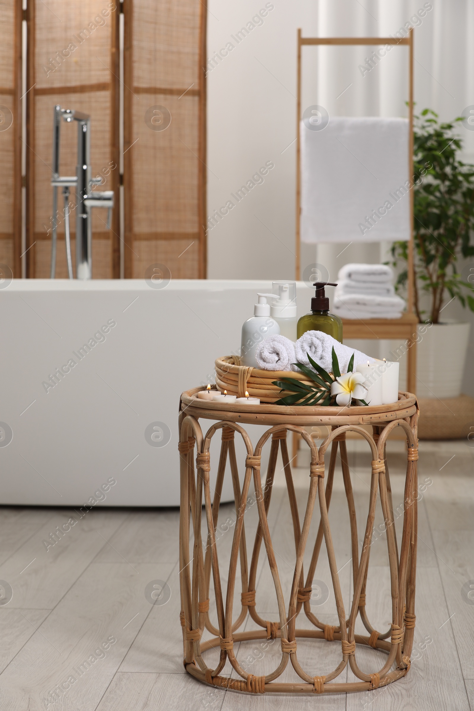 Photo of Spa products, burning candles, plumeria flower and tropical leaf on table in bathroom. Space for text