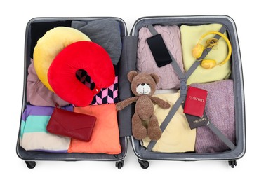 Soft travel pillows, headphones, passports and other items in open suitcase isolated on white, top view