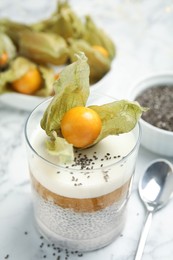Photo of Delicious chia pudding decorated with physalis fruit on white marble table, closeup