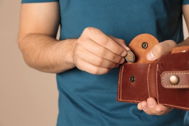 Photo of Young man putting coin into wallet on beige background, closeup. Space for text