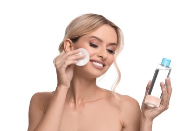 Photo of Smiling woman removing makeup with cotton pad and holding bottle on white background