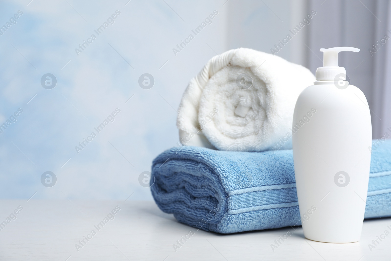 Photo of Bottle with shampoo and rolled bath towels on table, space for text