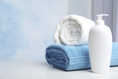 Photo of Bottle with shampoo and rolled bath towels on table, space for text