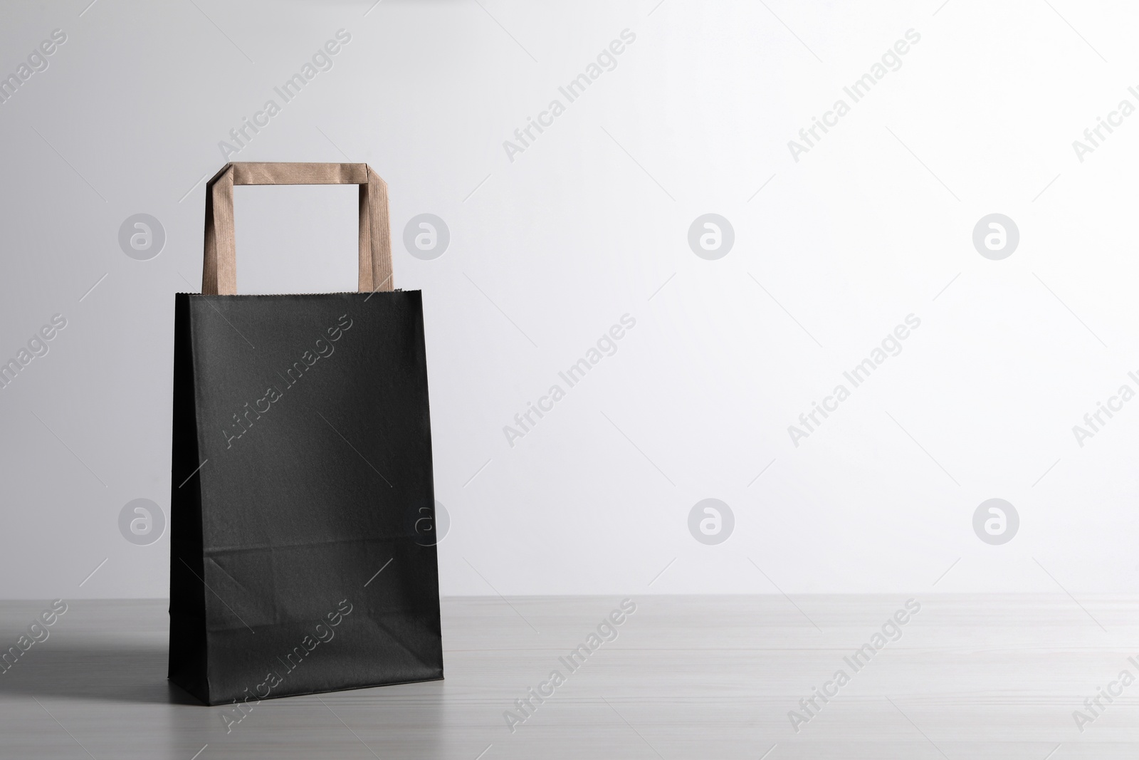 Photo of Black paper bag on white wooden table, space for text