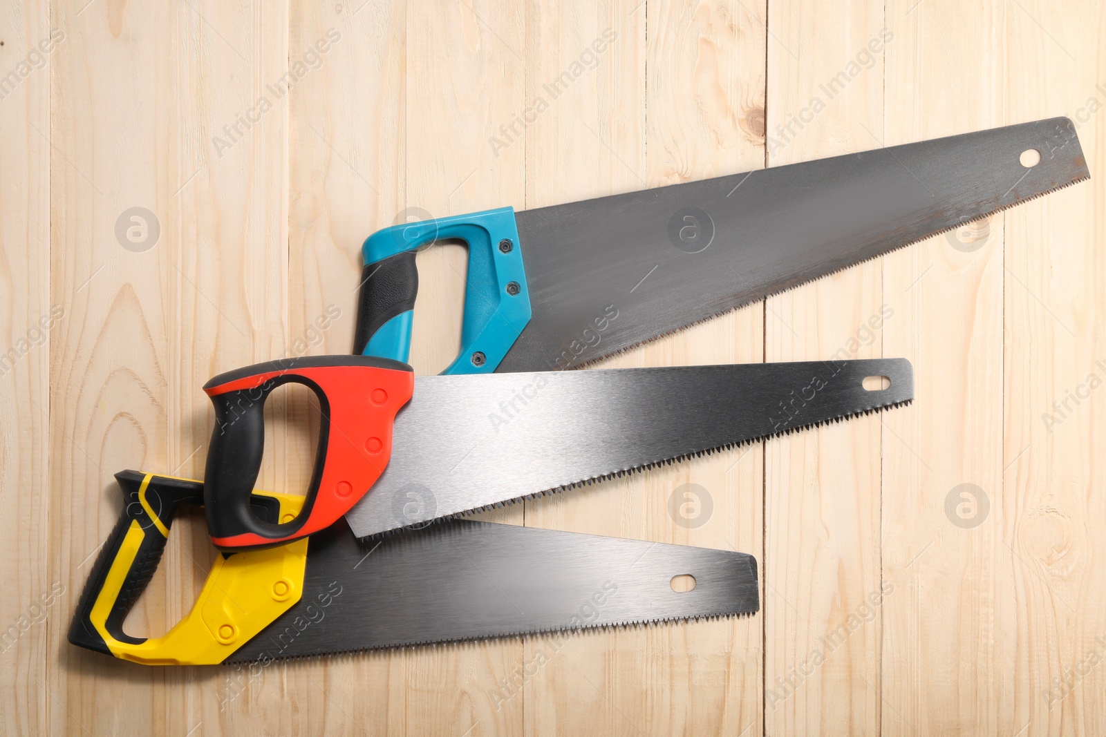 Photo of Saws with colorful handles on wooden background, flat lay