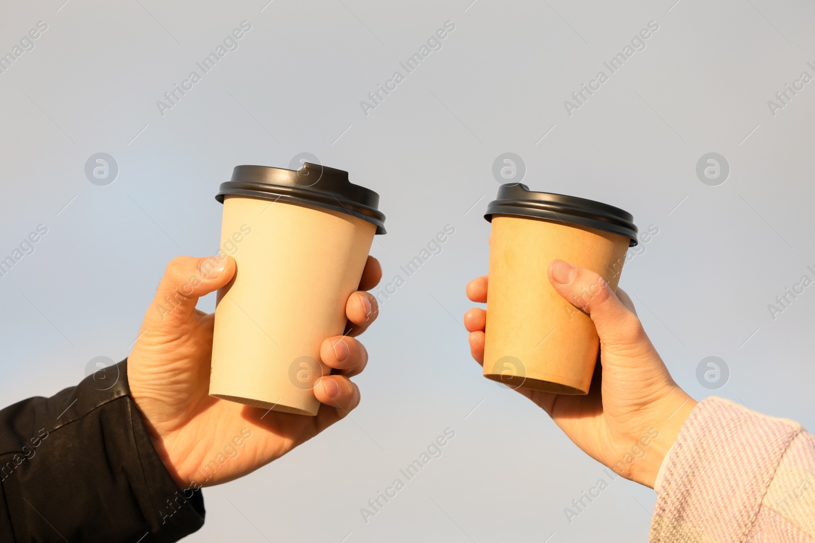 Photo of Man and woman holding paper coffee cups on blurred background, closeup