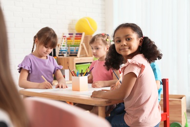 Photo of Adorable children drawing together at table indoors. Kindergarten playtime activities