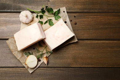 Photo of Tasty salt pork with herbs, onion and garlic on wooden table, flat lay. Space for text