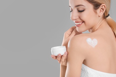 Young woman with jar of body cream on color background