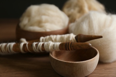 Photo of Spindles and soft white wool on wooden table, closeup