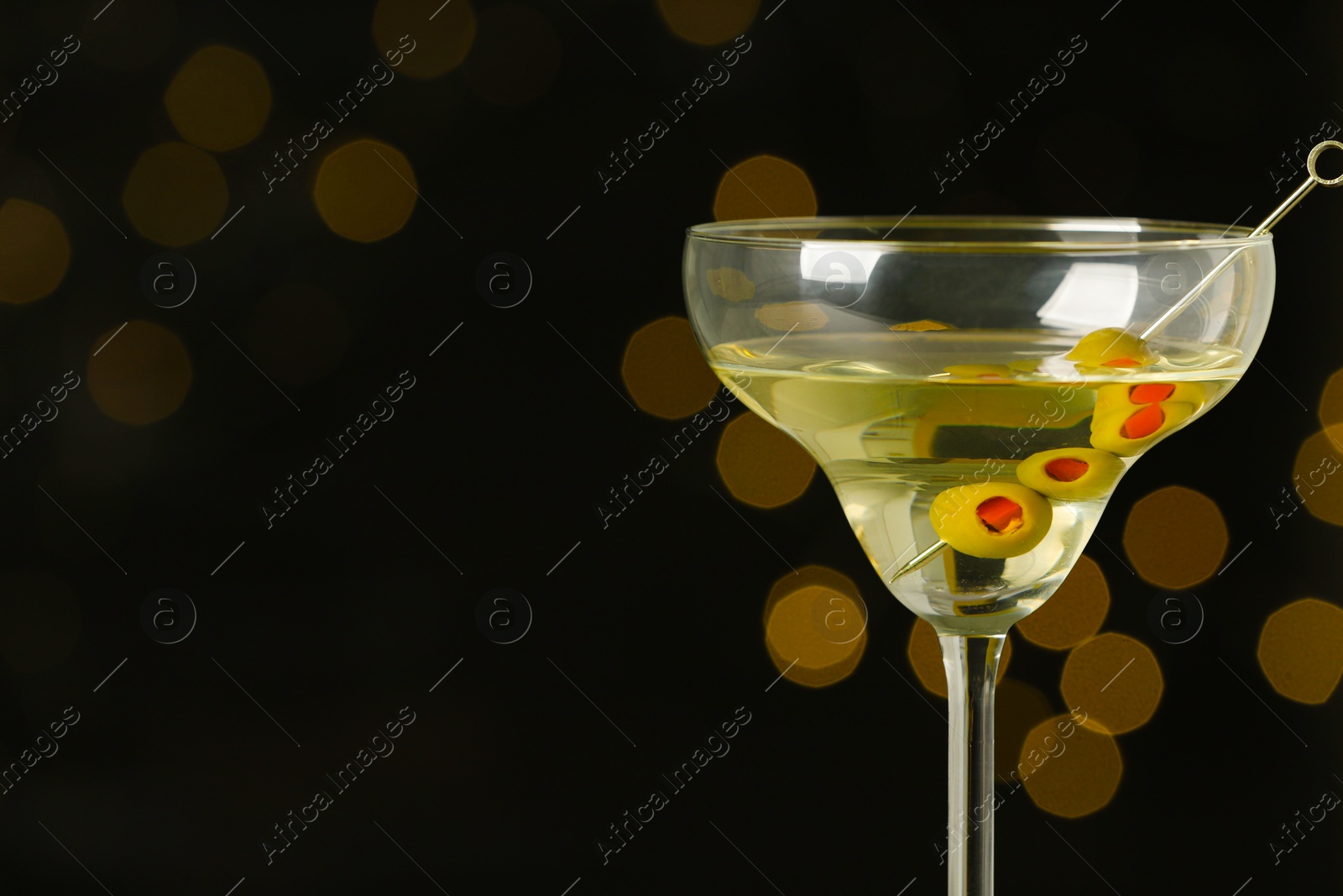 Photo of Glass of Classic Dry Martini with olives on blurred background. Space for text