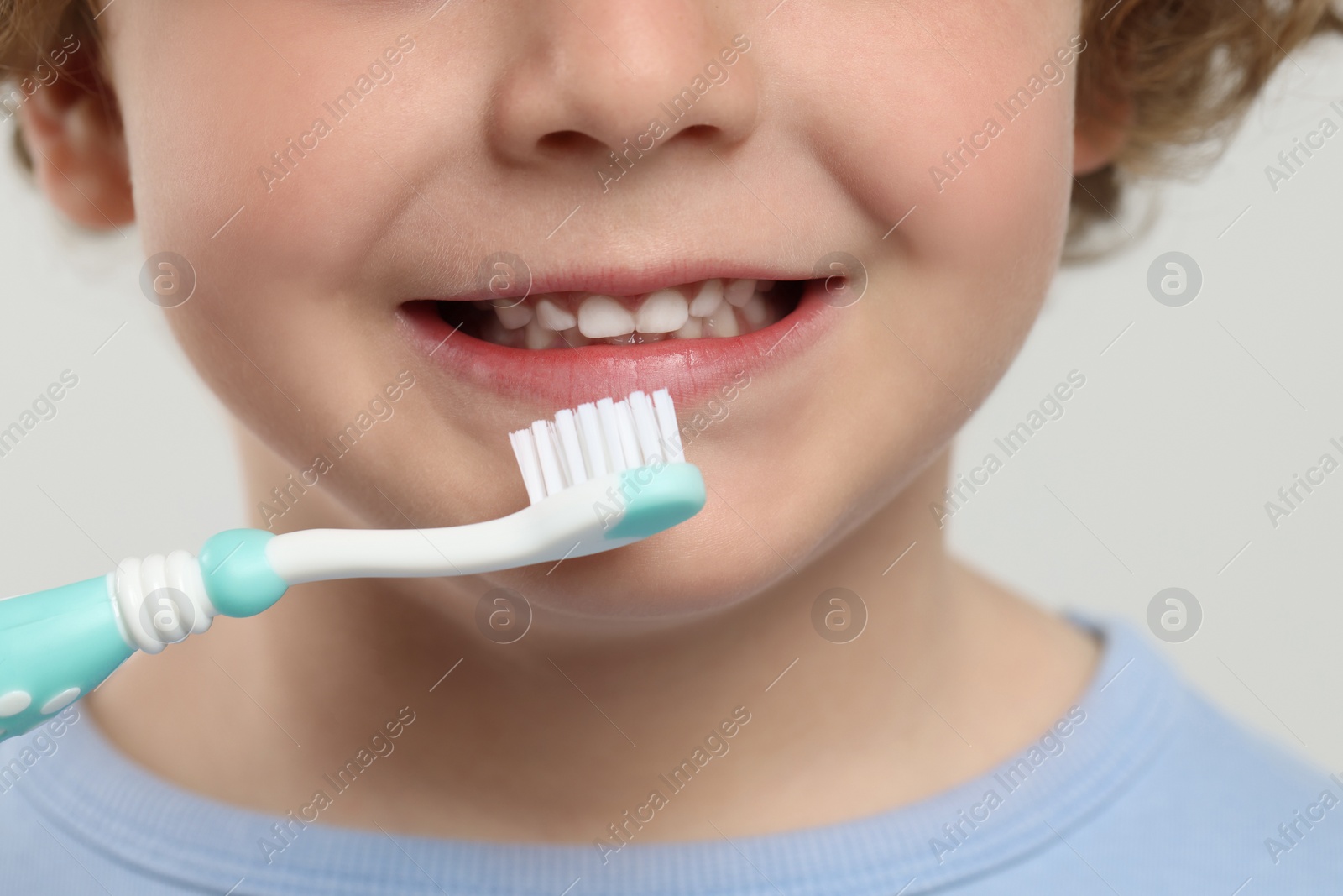 Photo of Cute little boy brushing his teeth with plastic toothbrush on white background, closeup