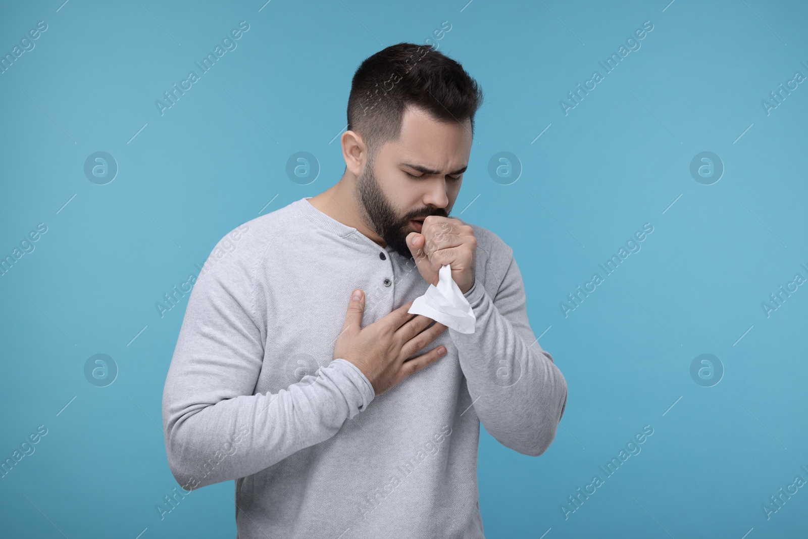 Photo of Sick man with tissue coughing on light blue background