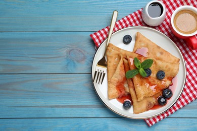 Photo of Delicious crepes served with blueberries, mint, syrup and cup of coffee on blue wooden table, flat lay. Space for text