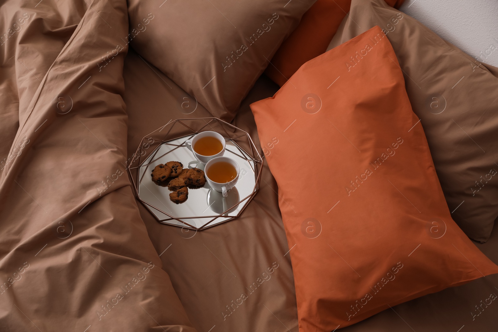 Photo of Cups of hot drink and cookies on bed with brown linens in stylish room, above view