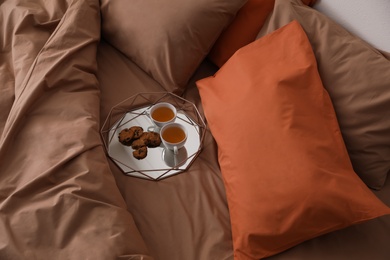 Cups of hot drink and cookies on bed with brown linens in stylish room, above view