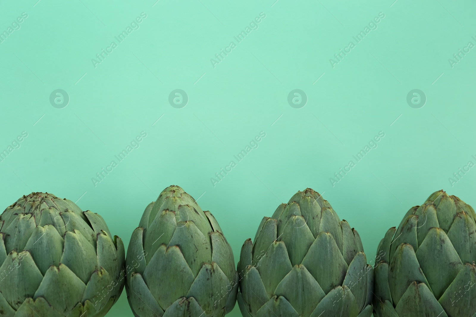 Photo of Whole fresh raw artichokes on green background, flat lay. Space for text