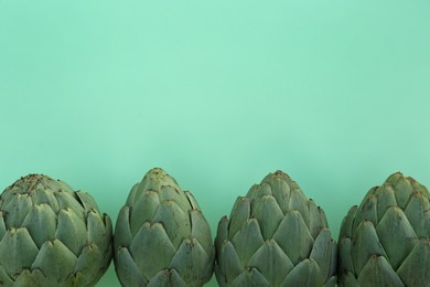 Photo of Whole fresh raw artichokes on green background, flat lay. Space for text