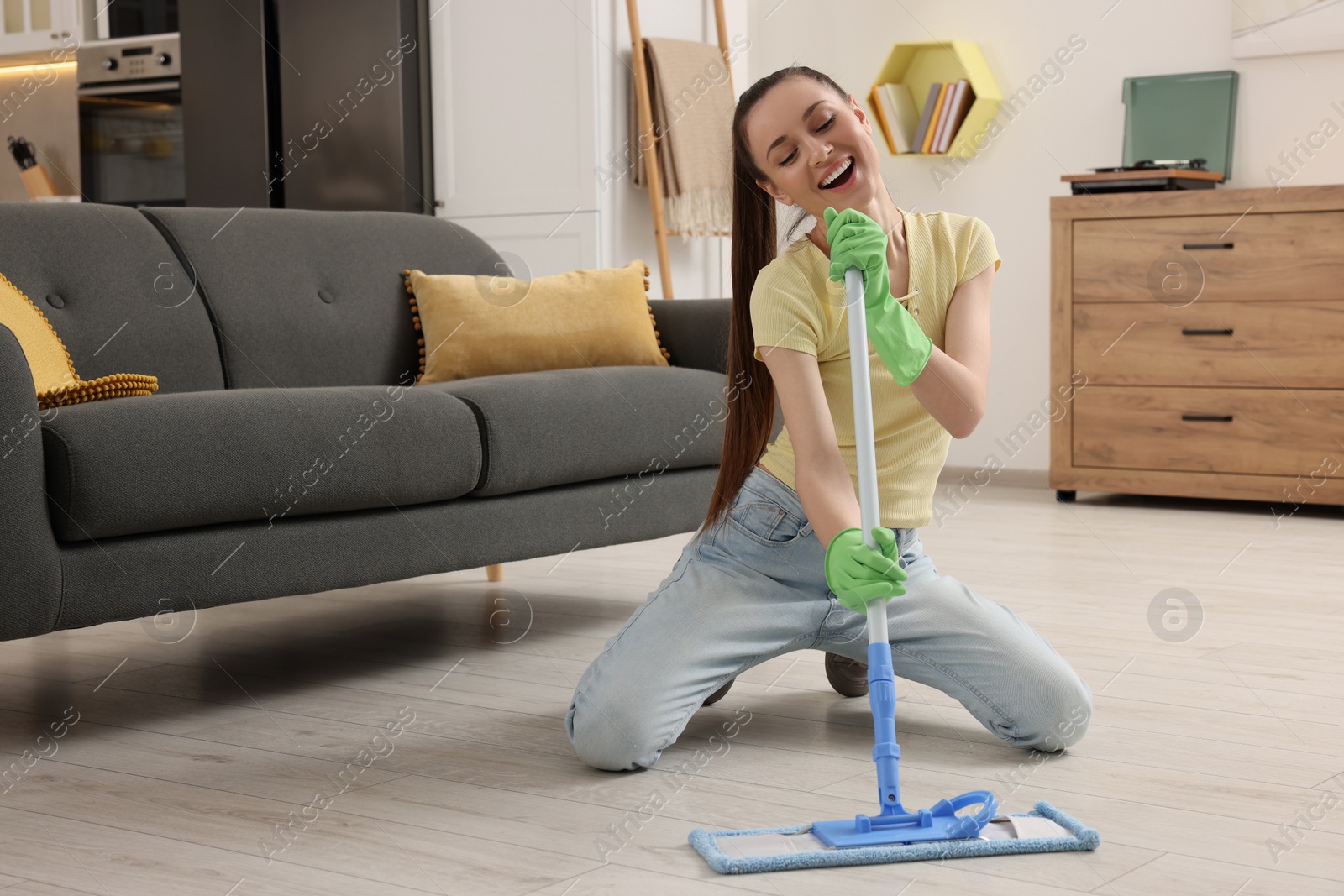 Photo of Spring cleaning. Young woman with mop singing while tidying up at home