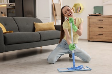 Photo of Spring cleaning. Young woman with mop singing while tidying up at home