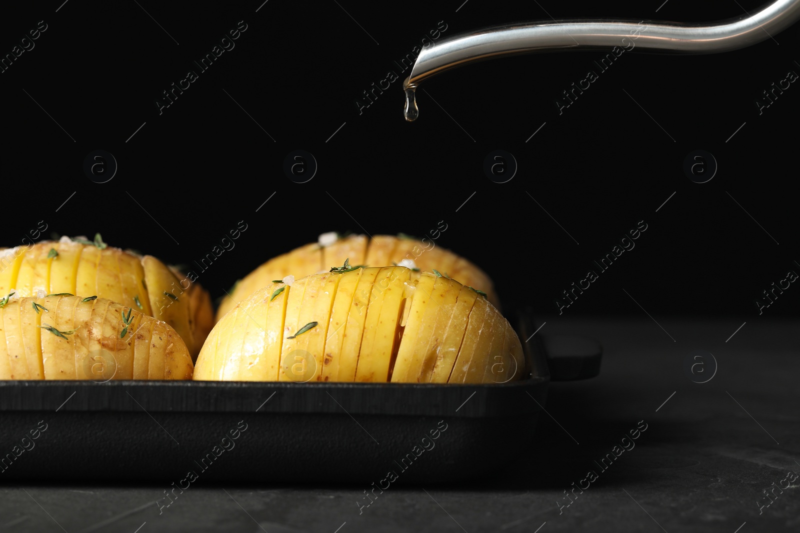 Photo of Oiling raw Hasselback potatoes before baking on dark grey table, closeup