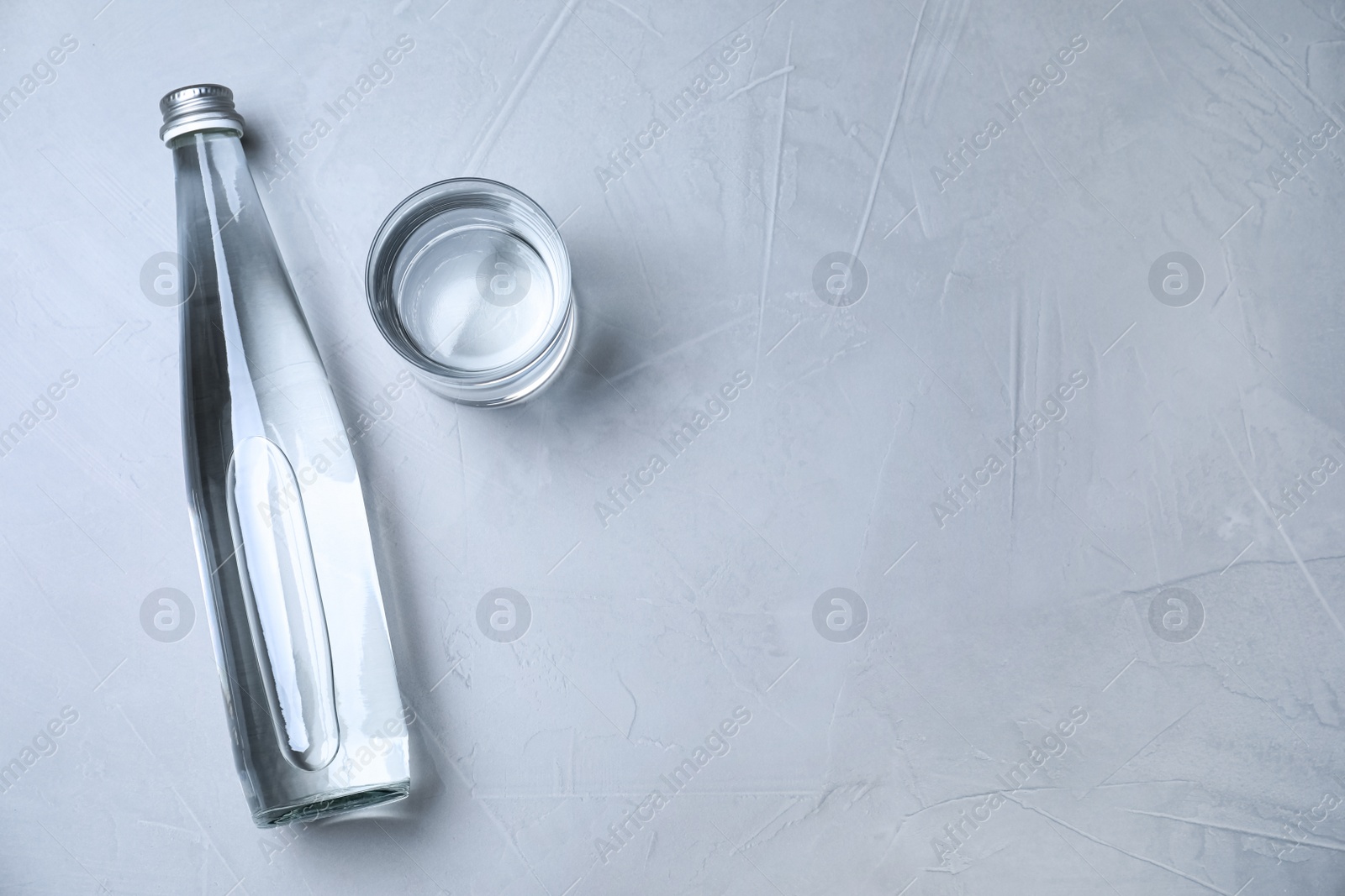 Photo of Glass and bottle with water on grey background, flat lay. Space for text