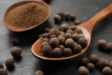 Photo of Ground and whole allspice berries (Jamaica pepper) on black table, closeup