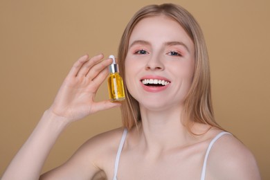 Photo of Beautiful young woman with bottle of essential oil on brown background