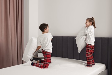 Photo of Brother and sister having pillow fight while changing bed linens in bedroom