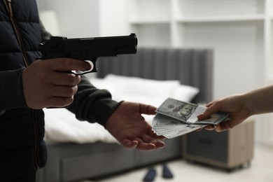 Woman giving money to criminal with gun indoors, closeup. Armed robbery