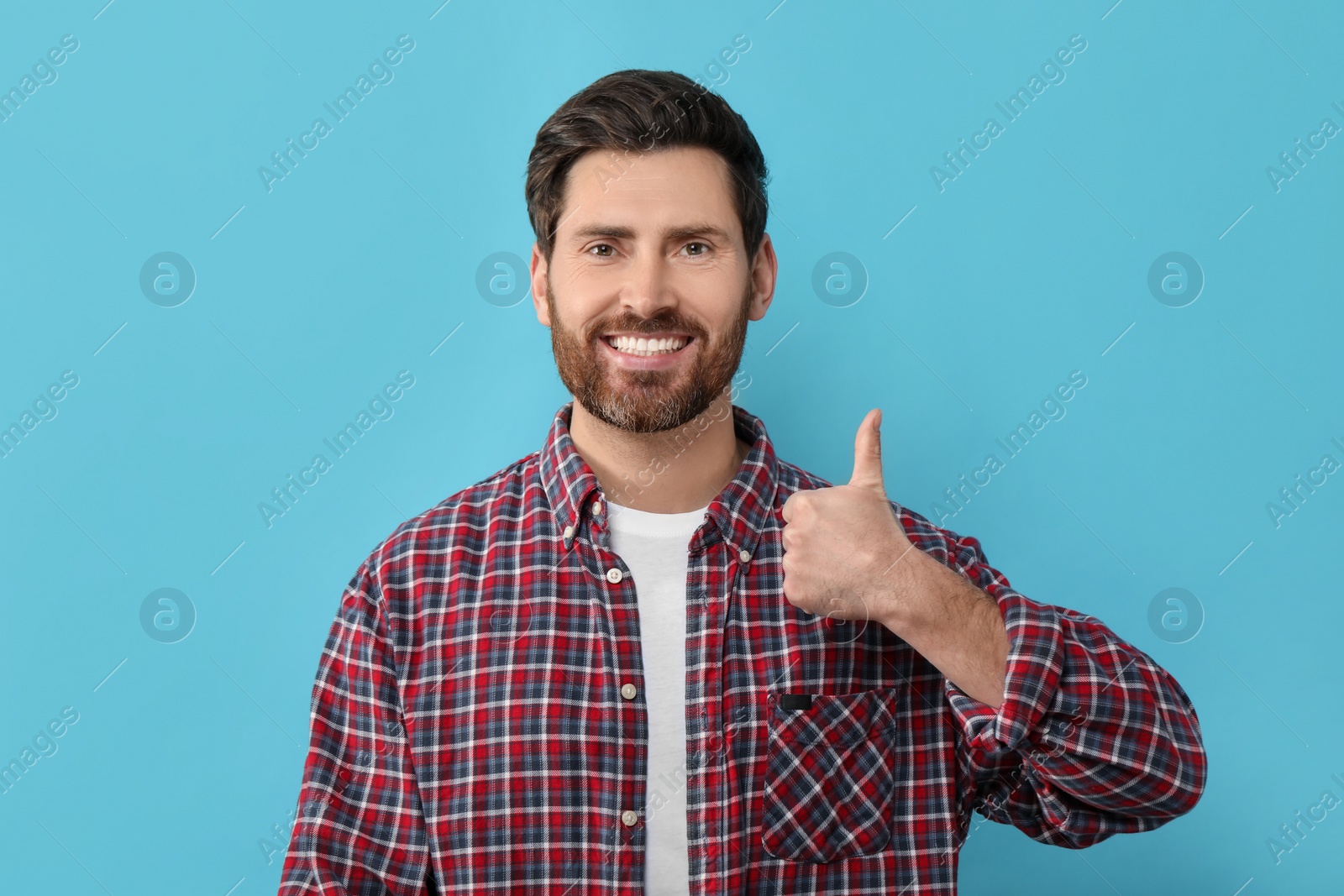 Photo of Portrait of smiling man with healthy clean teeth showing thumb up on light blue background