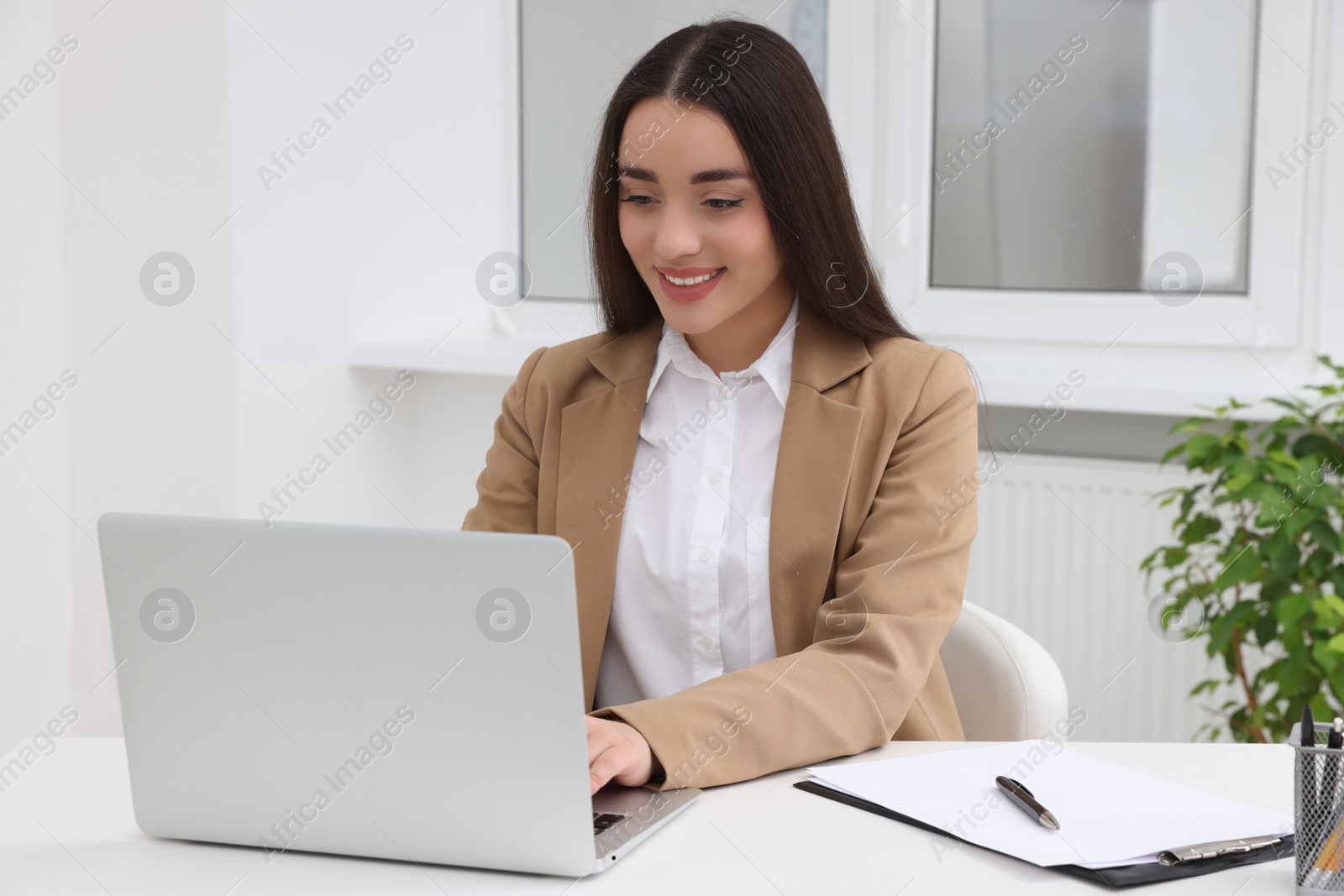 Photo of Young female intern working with laptop at table in office