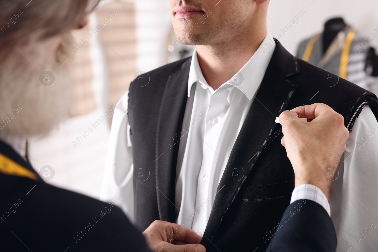 Photo of Professional tailor working with client in atelier, closeup