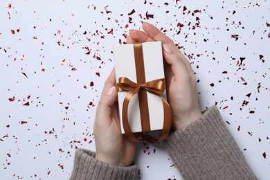 Photo of Christmas present. Woman with gift box and confetti on white background, top view