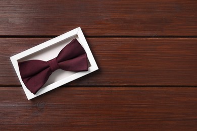 Photo of Stylish burgundy bow tie in box on wooden table, top view. Space for text