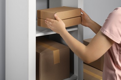 Photo of Woman putting cardboard box on shelf indoors, closeup. Packaging goods