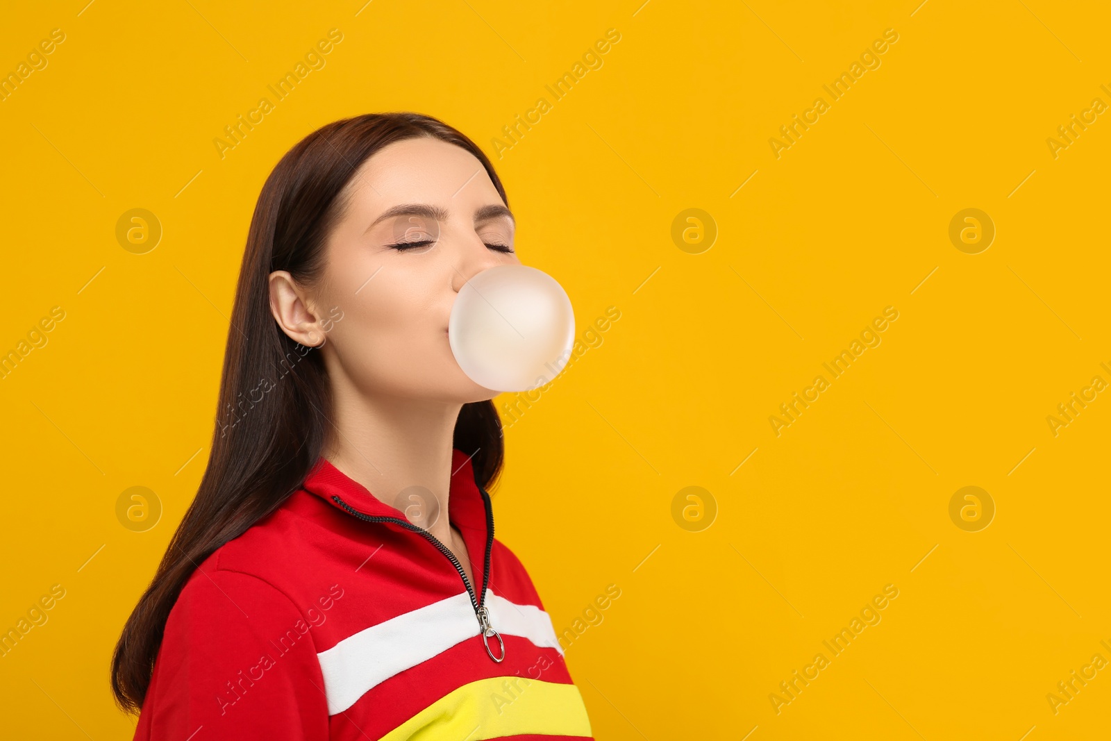 Photo of Beautiful woman blowing bubble gum on orange background, space for text