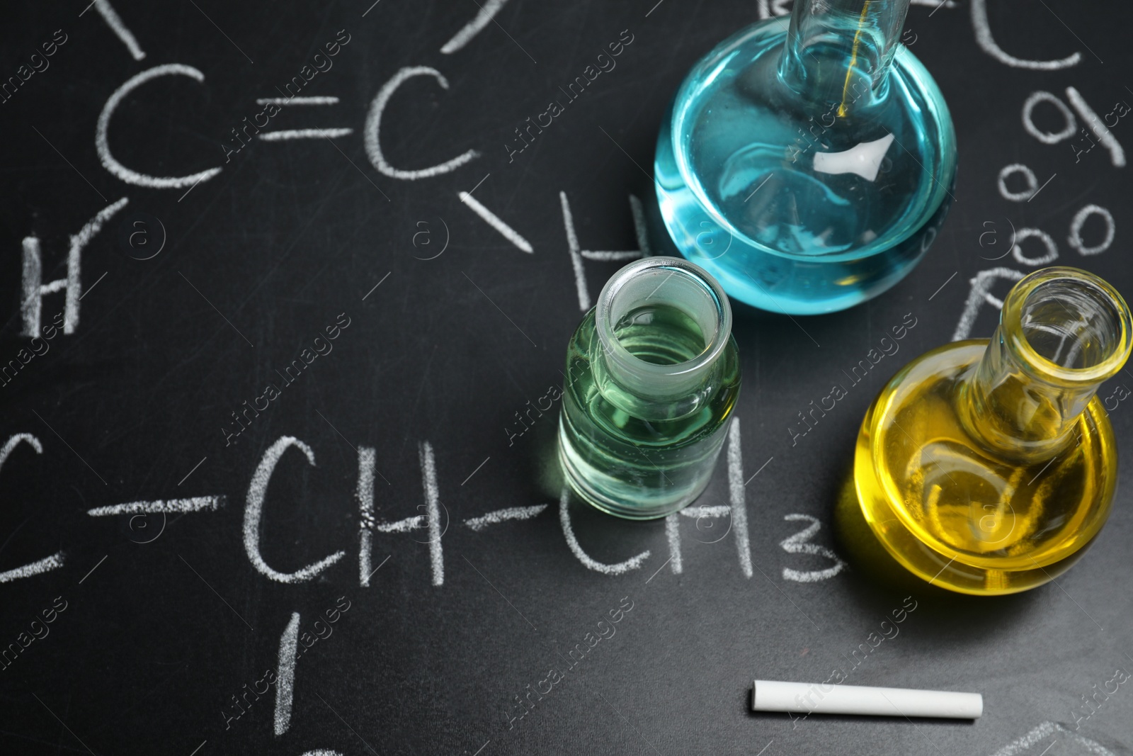 Photo of Laboratory glassware on blackboard with chemical formulas, closeup