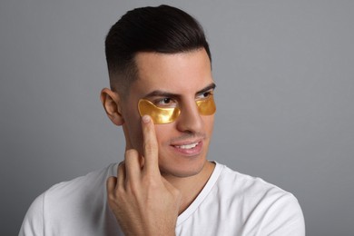 Photo of Man applying golden under eye patch on grey background