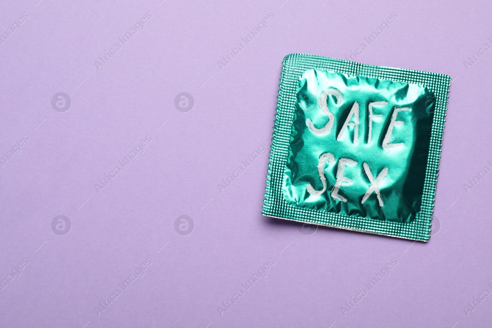 Photo of Green condom with phrase SAFE SEX on violet background, top view with space for text