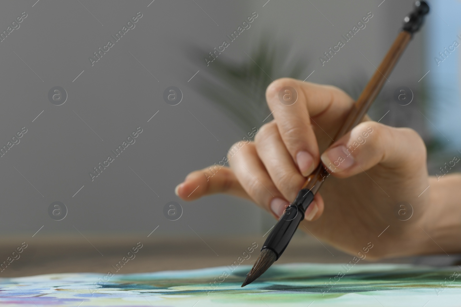 Photo of Woman painting with watercolor at table indoors, closeup. Space for text