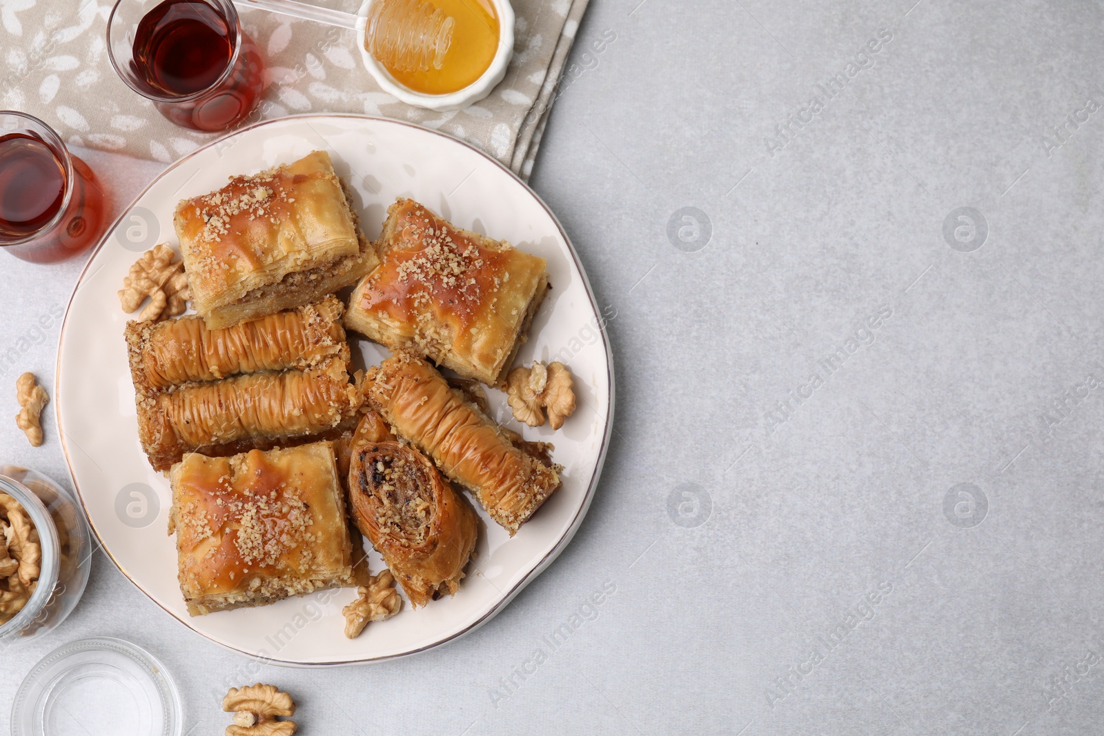 Photo of Eastern sweets. Pieces of tasty baklava, honey and tea on white table, flat lay. Space for text