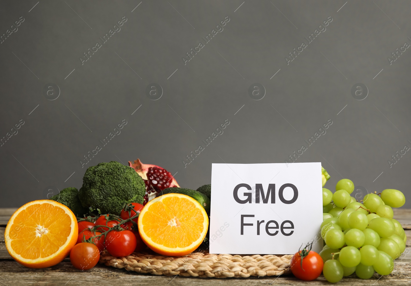 Photo of Tasty fresh GMO free products and paper card on wooden table against grey background